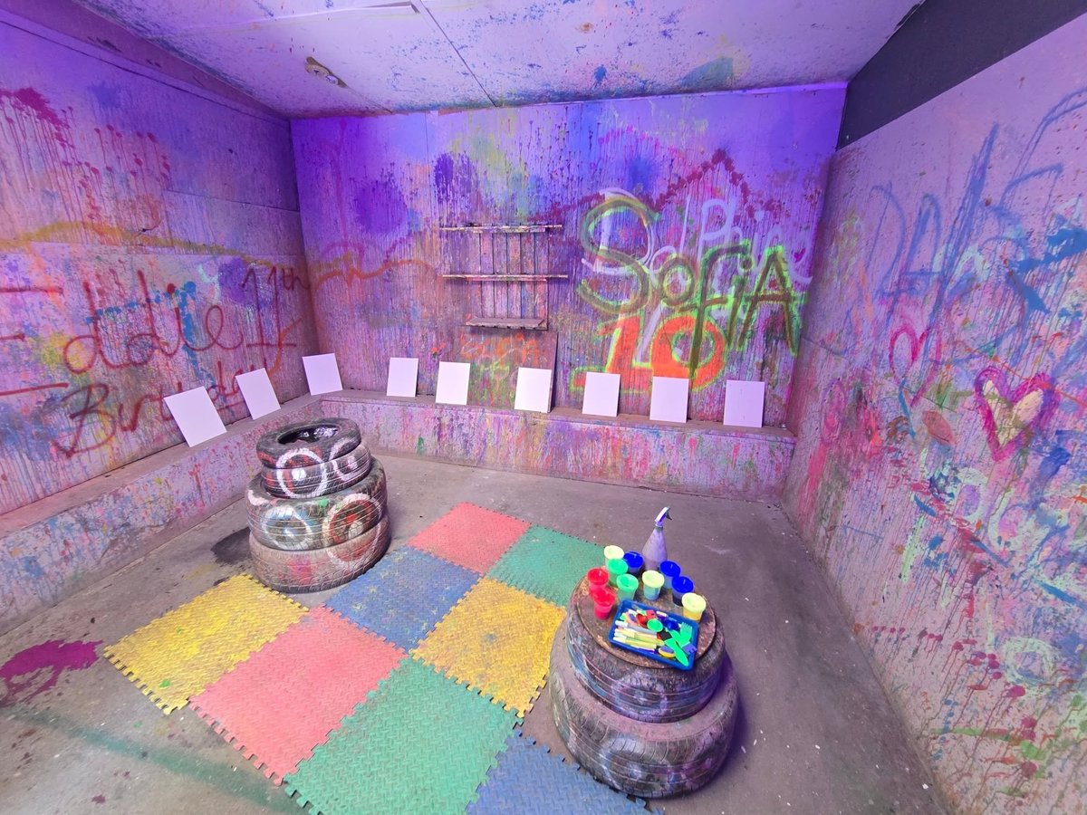 Colorful playroom with purple walls covered in graffiti art, foam floor mats in various colors, and sensory toys including a woven basket and colorful ball container