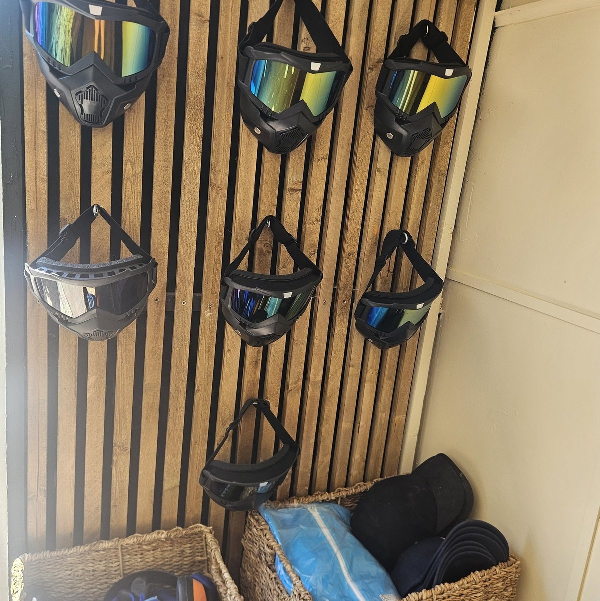 Collection of paintball masks displayed on wooden wall rack with storage baskets below